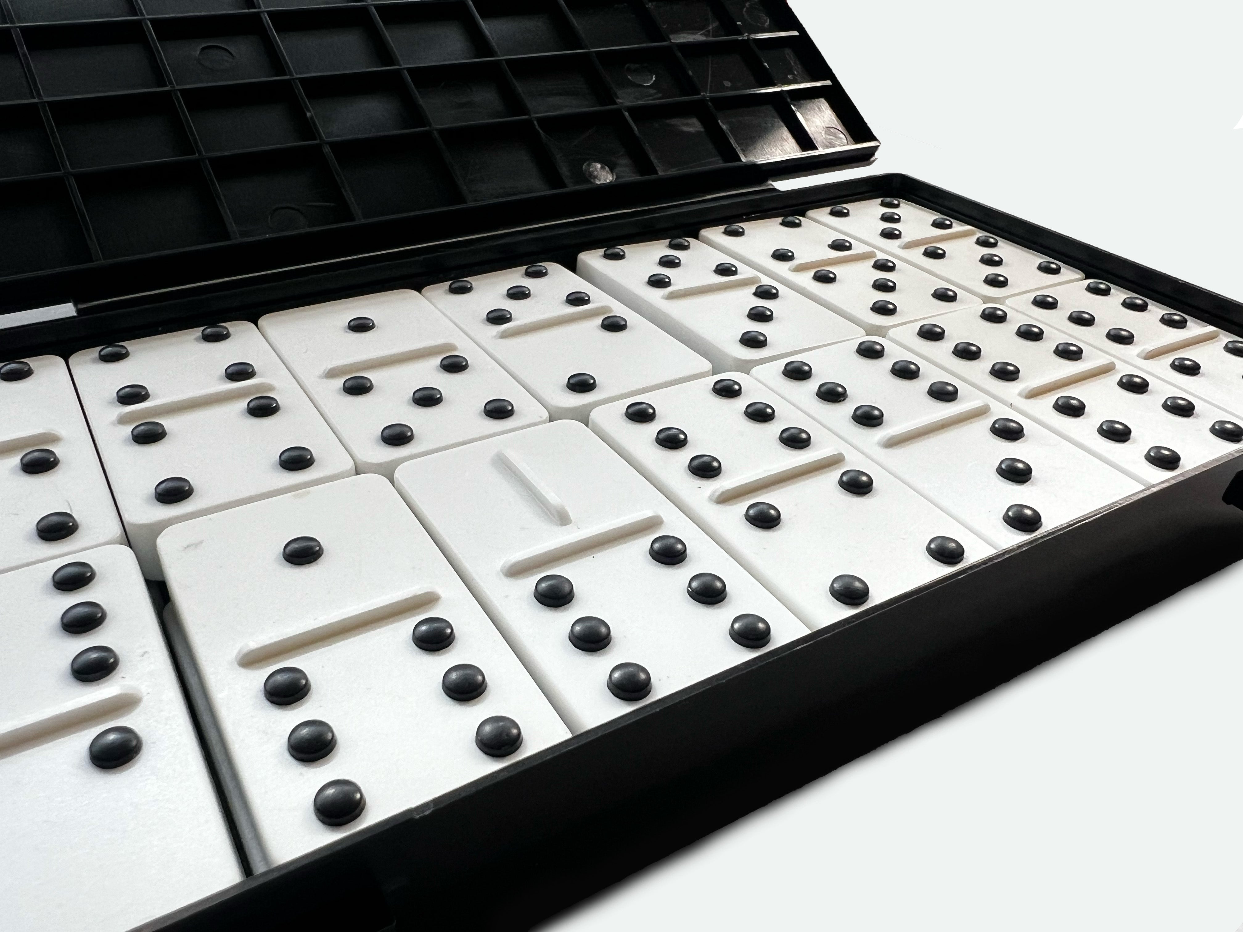 Primer plano de un estuche de dominós con puntos negros en relieve sobre fichas blancas, ordenados en filas dentro de su caja negra abierta.
